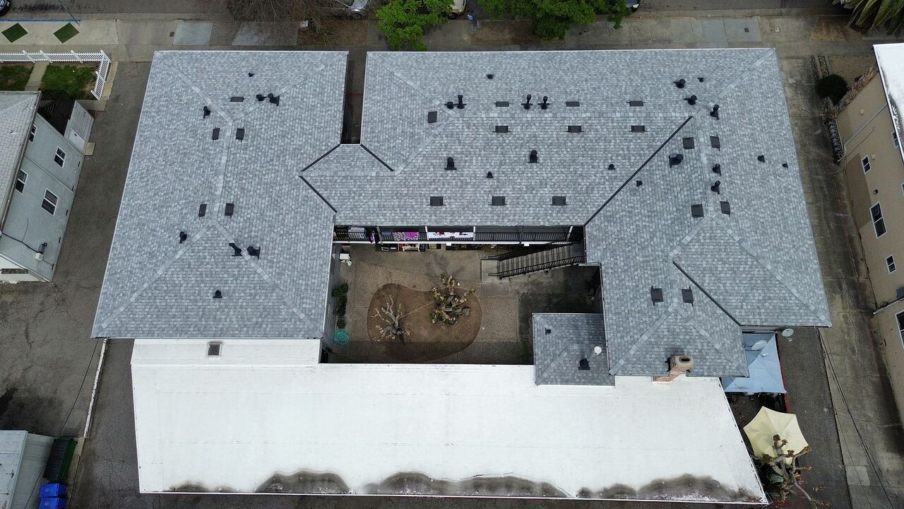 Aerial view of a finished San Jose apartment re-roof with Landmark shingles on the pitched wings and a single-ply membrane on the flat carport deck